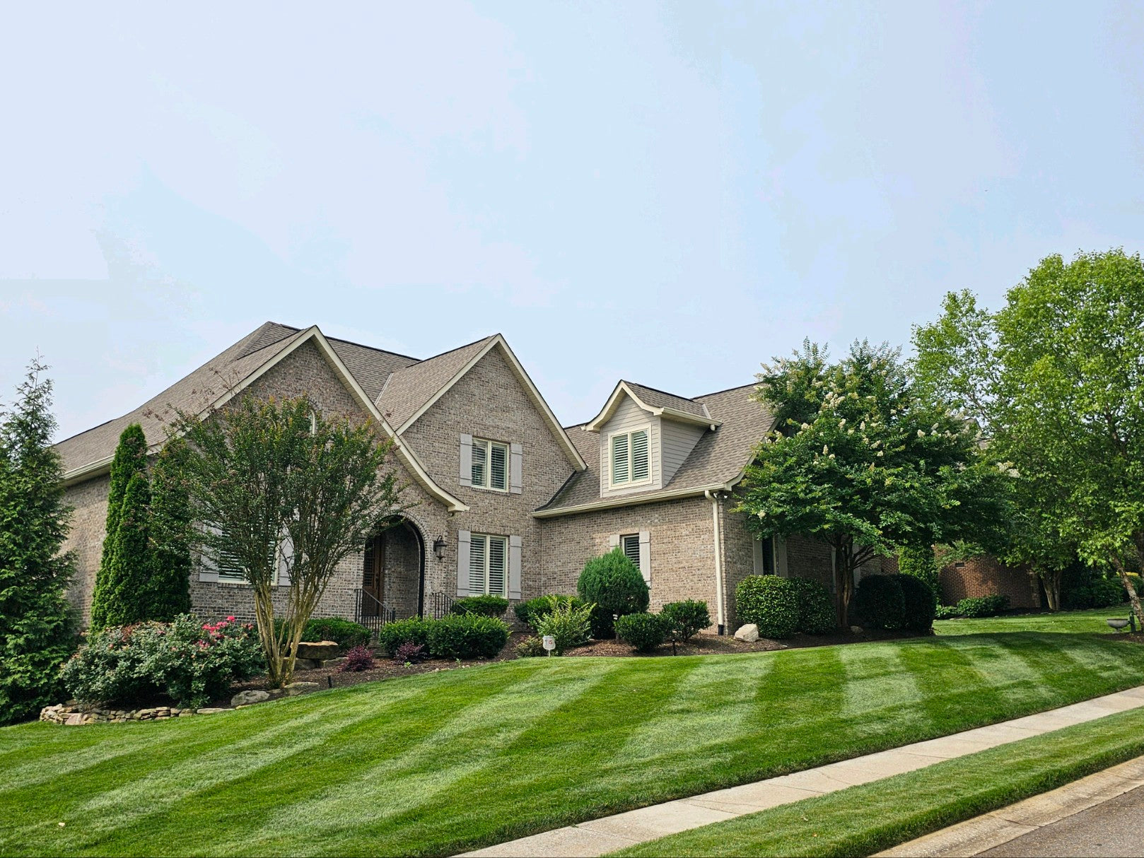 Gray brick house with neat landscaping, trimmed bushes, and newly cut and striped lawn.