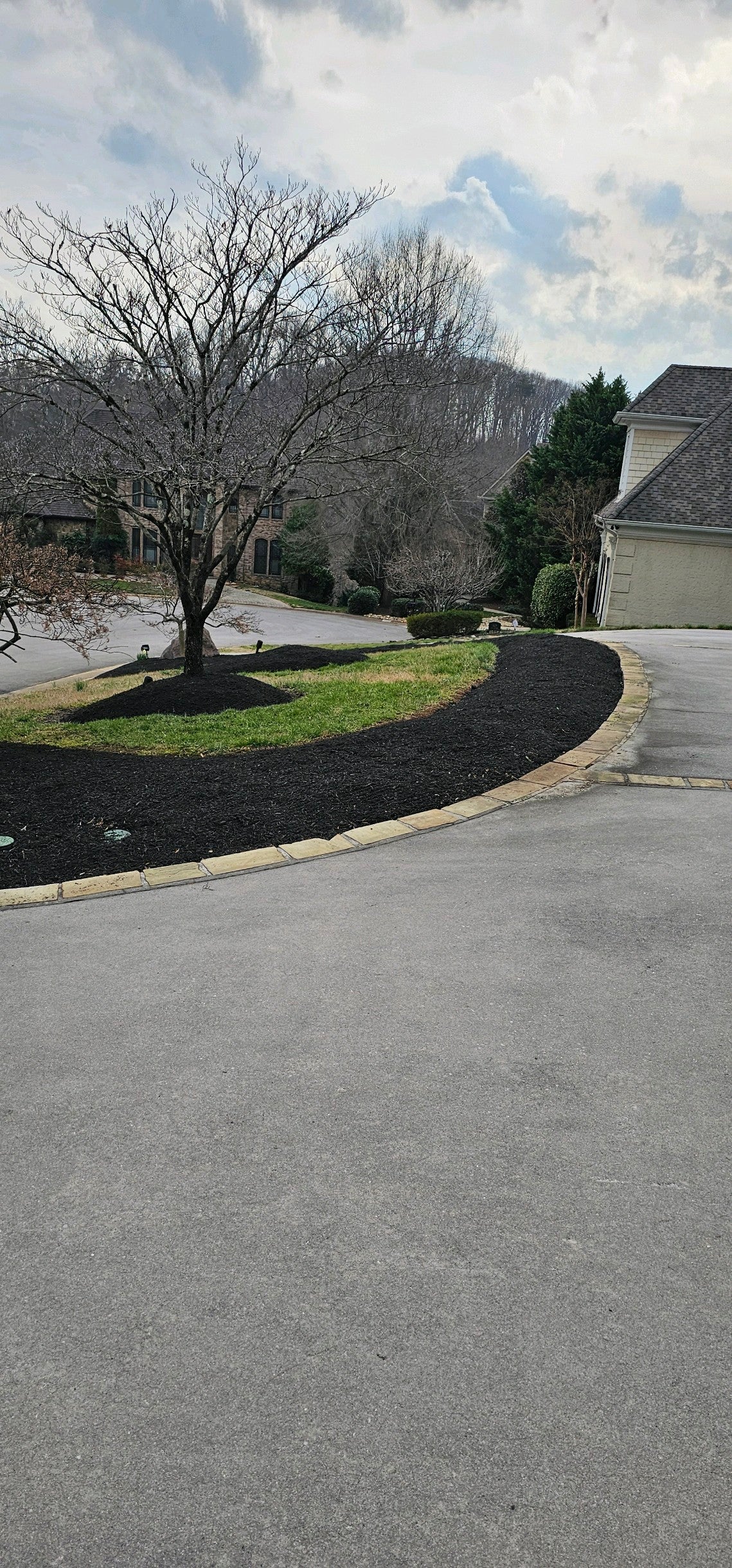 Circle driveway next to freshly mulched flower beds. No bushes. A few trees. Two houses in the background barely visable.