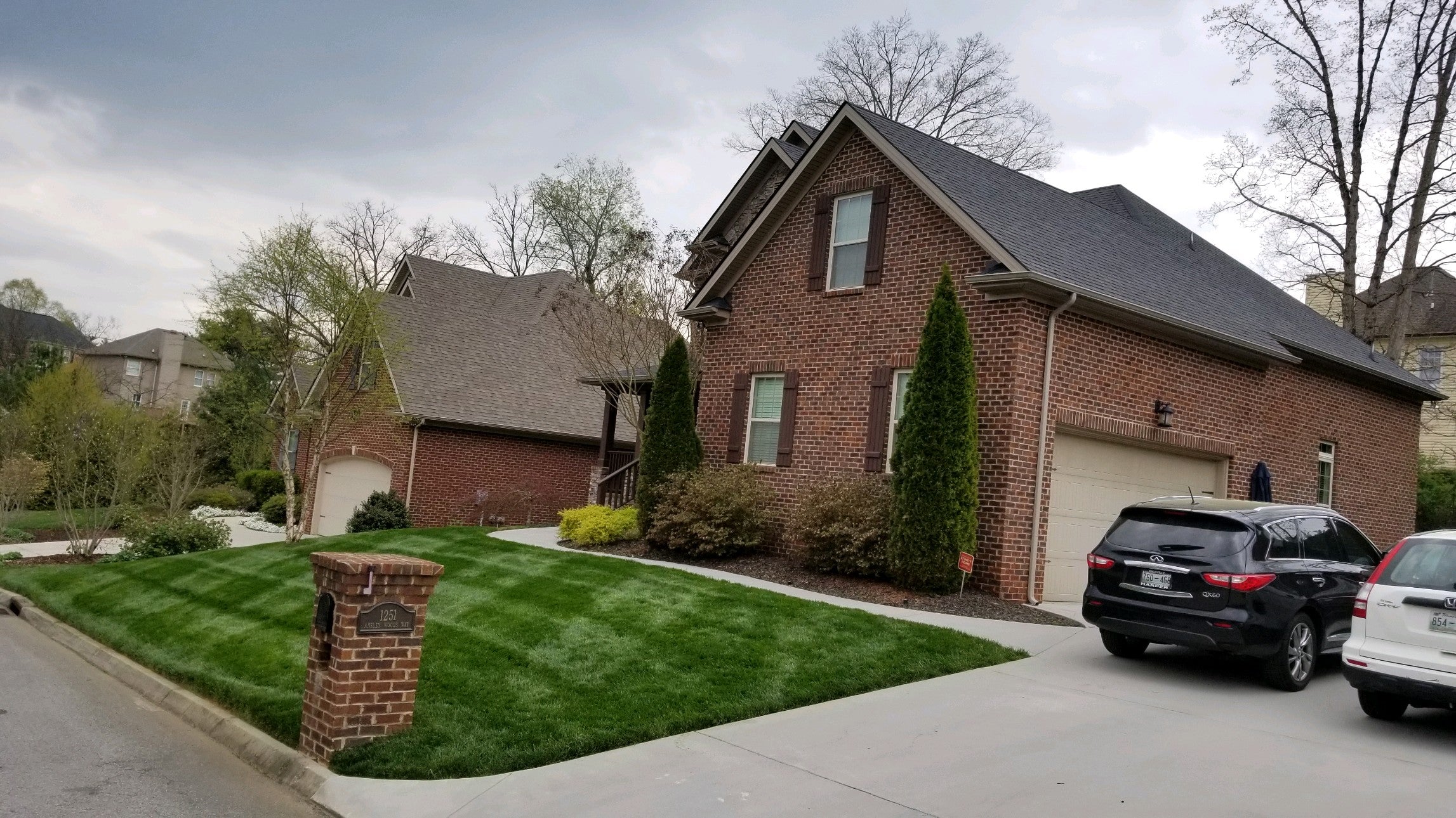 brick home  with two cars in driveway. freshly cut and striped lawn. A few trees in background.