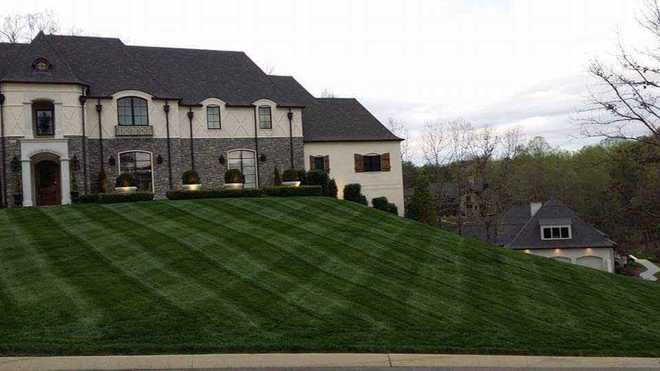 Large white and stone hosue on hill with beautifully cut and patterned lawn. Almost night time.