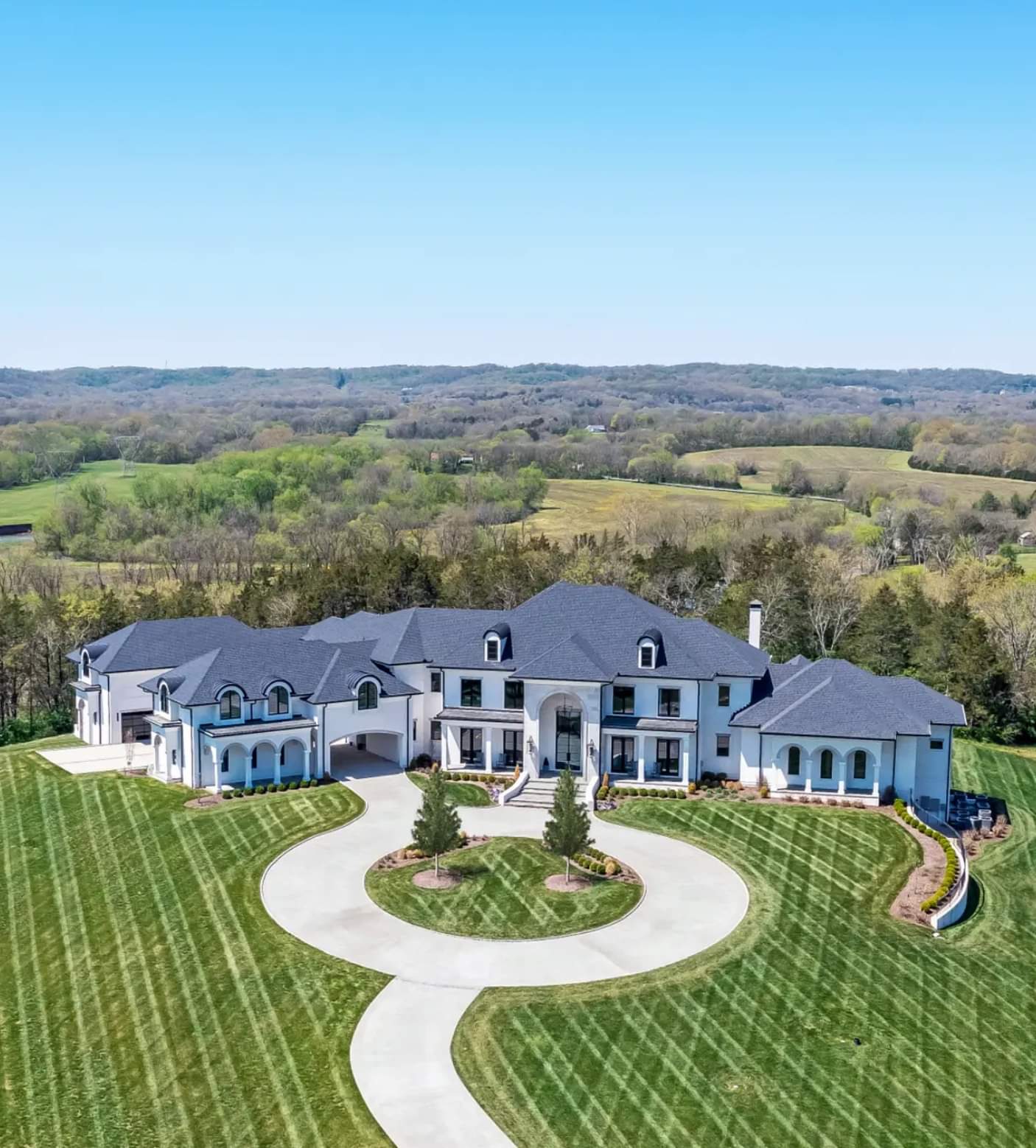 Enormous white house with beautifully and professionally mowed and patterned lawn.